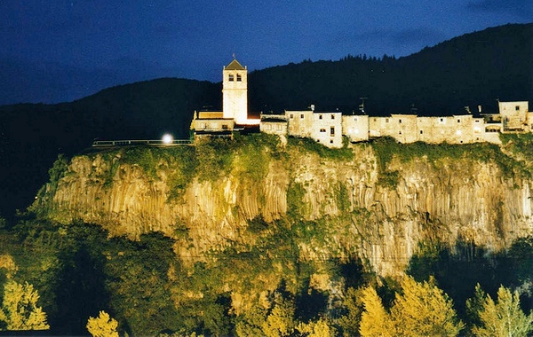 El pueblo de Castellfollit de la Roca, iluminado sobre la roca basáltica en las noches de verano. A la izquierda, el mirador Josep Pla.